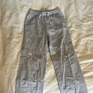 Randiga byxor från 157, stl 150 - Snygga och lätta byxor från 157 i storlek 150. De är ljusblå- och vitrandiga. Perfekta för chill dagar eller när du vill ha en avslappnad look.