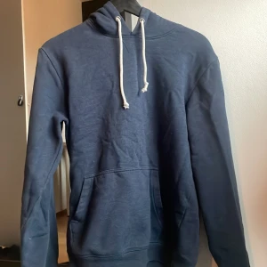 Mörkblå hoodie från Pier One - Mörkblå hoodie från Pier One med klassisk känguruficka och vita snören i huvan. Tröjan har lång ärm och en relaxed passform, perfekt för chill dagar. Tillverkad i mjuk bomullsmix som känns skön mot huden. Kontakta mig om ni har några funderingar!