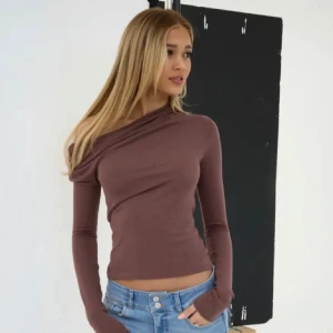 Brun oneshoulder croppad topp - Säljer en brun långärmad topp med oneshoulder-design och croppad passform. Toppen har en snygg asymmetrisk halsringning och sitter tight mot kroppen. Perfekt att styla med jeans eller kjol för en trendig look.