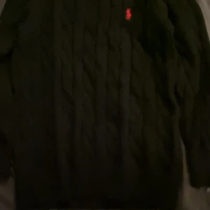 Svart kabelstickad tröja Ralph Lauren - Svart kabelstickad tröja från Ralph Lauren med klassisk röd broderad logga på bröstet. Tröjan säljs pågrund av för liten storlek 