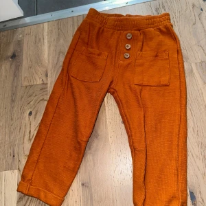 Orange manchesterbyxor LCW baby 18-24m - Snygga orange manchesterbyxor från LCW baby i storlek 18-24 månader. Byxorna har resår i midjan, tre dekorativa knappar framtill och två stora fickor. Perfekta för en cool och bekväm stil till de minsta.
