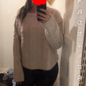 Vit kabelstickad tröja - Mysig vit kabelstickad tröja med lång ärm och rund hals. Tröjan har en loose passform och är perfekt för kyliga dagar. Snyggt stickat mönster som ger en klassisk och stilren look.