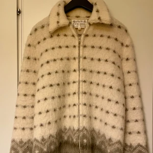 Isländsk ullkofta med dragkedja S -  Inköpt på Island. Retro a la 60 tal.  Använd fåtal ggr sedan hängt i garderob.  I mycket fint skick, inget att anmärka på.  Normal i storleken. Supermysig isländsk kofta i 100% ull från Karen Isull of Iceland. Koftan är vit med grått mönster och diskreta prickar, har lång ärm, hög krage och hel dragkedja framtill. Perfekt för kalla dagar och ger en riktigt cozy vibe.