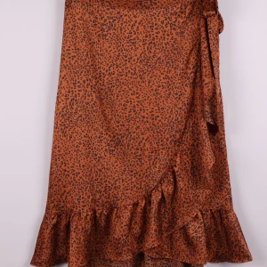 Leopardmönstrad omlottkjol Neo Noir - Snygg omlottkjol från Neo Noir i brunt med svart leopardmönster. Kjolen har volangkant nertill och knyts i sidan för en cool och trendig look. Perfekt för dig som vill sticka ut med ett djurmönster och gillar feminina detaljer.