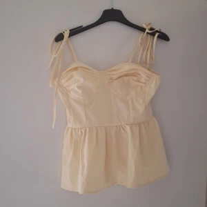 Ljusgul linnetopp med knytband - Supersöt ljusgul linnetopp med knytbara axelband och volang nertill. Aldrig använd men lappen är tyvärr bortklipt så vet ej vart den är ifrån eller storlek men skulle gissa S