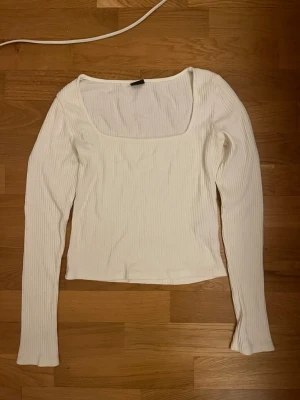 Vit ribbad långärmad topp Gina Tricot - Vit långärmad topp från Gina Tricot i ribbad bomullsmix. Toppen har en fyrkantig urringning och sitter figurnära. Perfekt att styla med jeans eller kjol för en clean look.
