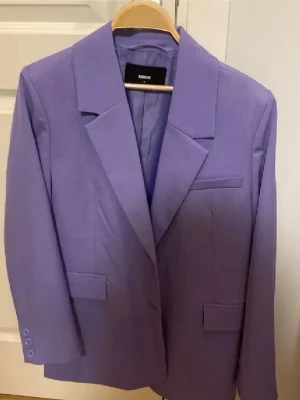 Lila kavaj från Bik Bok - Säljer en stilren lila kavaj från Bik Bok med klassisk krage och tre knappar vid ärmslutet. Kavajen har raka linjer, fickdetaljer och är helfodrad. Perfekt för dig som vill addera färg till din outfit.