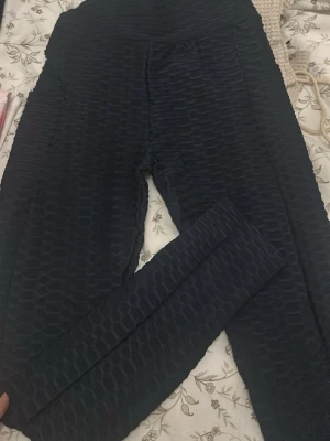 Mörk blå texturerade leggings - Säljer ett par svarta leggings med cool textur som ger en unik look. De är stretchiga och har hög midja, perfekta för att ge en snygg siluett. Materialet känns mjukt och följsamt mot huden, och mönstret gör dem extra intressanta. Passar dig som gillar att sticka ut.