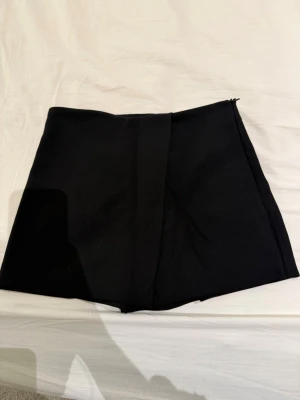 Svarta skorts från Zara, storlek S - Svarta skorts från Zara i storlek S. De har en stilren design med omlott framtill och dragkedja i sidan. Materialet är mjukt och har en lätt stretch, vilket gör dem bekväma att bära. Perfekta för dig som vill ha shorts med kjol-look.