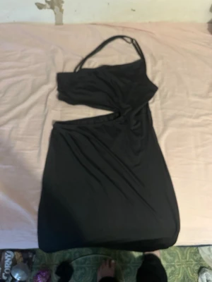 Svart långklänning med cut-out - Snygg svart långklänning med ett trendigt cut-out parti i midjan och smala axelband. Klänningen har en oneshoulder-design och är figurnära med mjukt, stretchigt material som ger en cool och modern look.