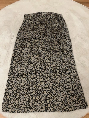 Leopardmönstrad långkjol från ONLY - Snygg långkjol från ONLY i beige och svart leopardmönster. Kjolen har en rak passform och är tillverkad i ett typ silkes, glansigt material som känns lyxigt. Perfekt för dig som vill sticka ut med ett djurmönster och ändå hålla det stilrent.