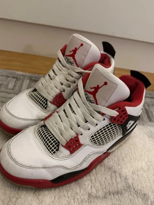 Nike Air Jordan 4 fire red retro - Kan passa som 40 med Nike Air Jordan 4 Retro sneakers med vit ovandel i skinn, röda och svarta detaljer samt meshpaneler på sidorna. Klassisk Jumpman-logga på plösen och Nike Air-logga på hälen. Skorna har snörning och en platt sula med synlig Air-enhet.