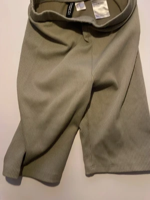 Ribbade cykelshorts från divided  - Säljer ett par beige/gröna shorts från divided med smala vertikala ränder. De har en relaxed passform och är tillverkade i ett mjukt material som känns skönt mot huden. Perfekta för varma dagar och har en stilren look som funkar till många outfits.