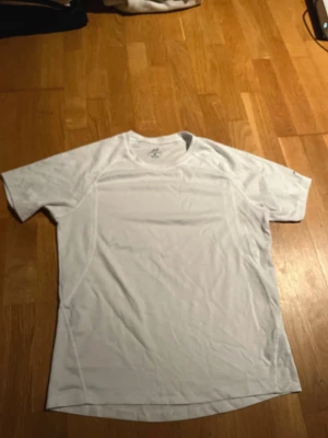 Vit tränings-tshirt från Pro Touch - Säljer en vit t-shirt från Pro Touch i storlek S, perfekt för träning. Materialet är lätt och andas, med diskret logga på ärmen och vid halsen. T-shirten har rund hals och korta ärmar, tillverkad i syntet för att transportera bort fukt. Liten fläck på magen