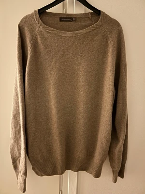 Beige stickad tröja från Oscar Jacobson - Säljer en beige stickad tröja från Oscar Jacobson med rund hals och ribbade muddar vid ärmslut och nederkant. Tröjan har en enkel och klassisk design.