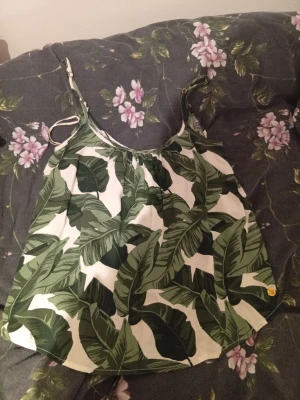 Grön och vit linnetopp Pernilla Wahlgren - Säljer en snygg linnetopp från Pernilla Wahlgren i storlek XS. Toppen har tropiskt bladmönster i grönt och vitt, tunna justerbara axelband och luftig passform. Perfekt för varma dagar och sommarhäng. Materialet känns lätt och skönt mot huden.