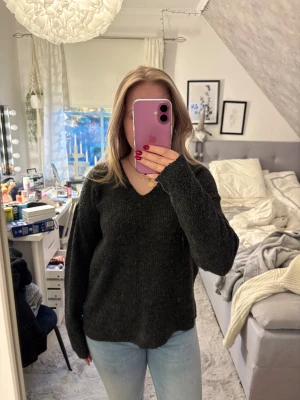 Mörkgrå stickad tröja med v-ringning - Mysig mörkgrå stickad tröja med v-ringad hals och långa ärmar. Perfekt för kyliga dagar och enkel att matcha med jeans eller kjol. Tröjan har en loose passform och är tillverkad i ett mjukt stickat material som känns skönt mot huden.