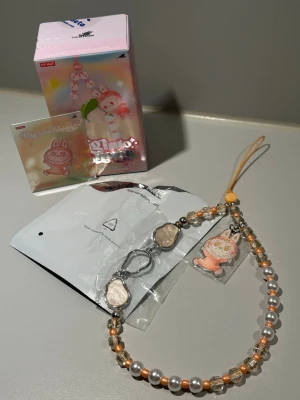 PopMart Labubu Big Into Energy Phone Charm - Happiness - Otroligt fint smycke för mobil, väska eller nyckelring. Rött och rosa med skimrande berlocker. Smycket håller hög kvalitet, väldigt hållbar då den inte är elastisk.  Smycket är helt nytt, detaljer och kort är fortfarande förseglat.