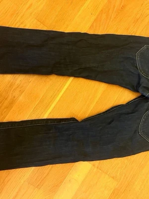 Replay jeans mörkblå bootcut - Snygga mörkblå jeans från Replay med bootcut-snitt och råa, fransiga benslut. Klassisk femficksdesign, silverfärgade detaljer och tydliga Replay-loggor på knapp och ficka. Jeansen är gjorda i slitstarkt denim och har kontrastsömmar.