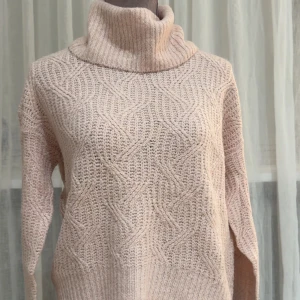 Baby rosa stickad polotröja - Säljer en baby rosa stickad polotröja med snyggt strukturmönster. Tröjan har hög krage och långa ärmar, perfekt för kyliga dagar. Den är ribbstickad vid kragen och nederkanten vilket ger en schysst detalj. Använt ett fåtal gånger. 