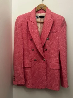 Rosa kavaj från Zara med knappar stl.S - Säljer en snygg rosa kavaj från Zara med dubbelknäppning och markerade axlar. Kavajen har en strukturerad yta, klassisk krage och fickor framtill. Metallknappar på framsidan och vid ärmslut ger en cool touch. Perfekt för dig som vill sticka ut med färg. Stl. S