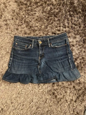 Mörkblå jeanskjol med volangkant - Supersnygg mörkblå jeanskjol från Levi's med volangkant nedtill och klassiska fickor både fram och bak. Kjolen har en normal passform och coola kontrastsömmar. Perfekt för dig som gillar denim och vill ha en kort kjol med lite extra detalj. Egensydd