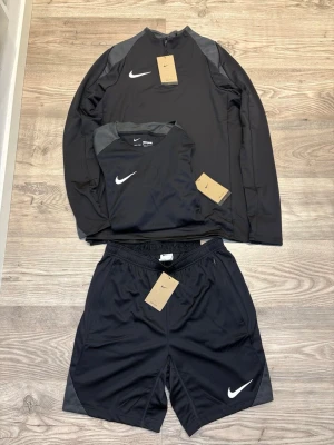 Nike Set - Nike Set i svart färg med vit Nike Swoosh. 3 delar long sleeve, t-shirt & shorts. Storlek: M. Perfekt för chill dagar hemma eller träning.