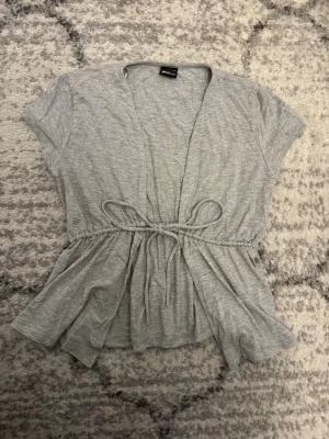 Grå knytblus Gina Tricot  - Säljer en fin grå kortärmad knytblus från Gina Tricot i storlek S. Blusen har knytning i midjan och v-ringning. Annars är den i jätte fint skick i gott som ny och använd endast en gång. Säljer för 139kr pga att den är i så fin standard och är ny. 