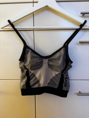 Grå och svart topp från Iets Frans Urban Outfitters - Säljer en croppad topp från Iets Frans Urban Outfitters i grått och svart med tunna axelband. Toppen har ribbade kanter, rynkade detaljer framtill och logga på ryggen. Nyskick!