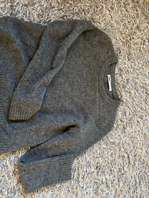 Grå stickad tröja från Zara - Mysig grå stickad tröja från Zara i storlek S. Tröjan har rund halsringning och långa ärmar med ribbade muddar.