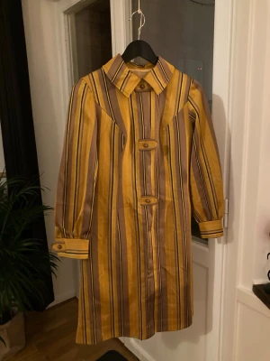 Klänning RETRO - Gul/brun/orange retor-klänning i toppenskick säljes för 200kr i storlek 36/38. Det finns ett litet hål i fodret längst bak i nacken som enkelt går att laga. Hålet kan lagas av mig på beställning vid köp av klänningen utan extra kostnad. 