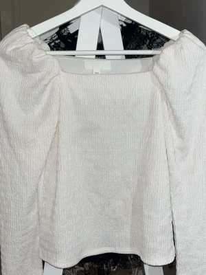 Vit långärmad topp från H&M - Säljer en vit långärmad topp/blus från H&M med puffiga axlar och strukturerat tyg. Fyrkantig ringning som ger en trendig look. Sparsamt använd! ⭐️.