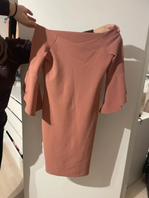 Rosa klänning med volangärm River Island - Säljer en snygg rosa klänning från River Island i storlek 10. Klänningen har volangärmar och en figurnära passform med offshoulder-design. Materialet känns mjukt och har lite stretch. Perfekt för dig som gillar stilrena detaljer och vill sticka ut med volangärmar.