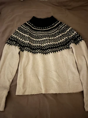 Mönstrad stickad tröja från H&M XS - Säljer en stickad tröja från H&M i storlek XS. Tröjan är vit med svart mönster över axlar och bröst, har lång ärm och ribbade muddar. Perfekt för kyliga dagar och har en klassisk nordisk vibe med sitt grafiska mönster.