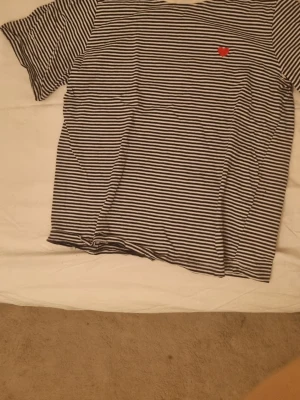 Randig t-shirt med hjärtdetalj JDY - Säljer en svartvit randig t-shirt från JDY i storlek S. T-shirten har korta ärmar och ett litet rött hjärta broderat på bröstet. Materialet känns som mjuk bomull och passformen är normal. Perfekt för dig som gillar enkla men snygga detaljer.