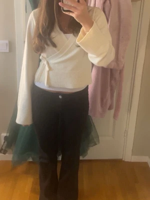 Vit omlottopp med knyt och vida ärmar - Säljer en vit omlottopp med knyt i sidan och breda, långa ärmar. Toppen är croppad och har ribbade detaljer vid ärmslut och nederkant. Perfekt för dig som gillar en stilren och trendig look.