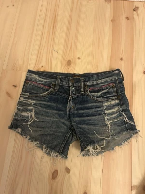 Blå slitna jeansshorts Washborn S - Säljer ett par blå jeansshorts från Washborn i storlek S. De har fransiga kanter, slitna detaljer och coola broderier på bakfickorna. Fickorna har färgglada tygdetaljer och nitar. Shortsen är gjorda i 100% bomull och har normal/ lowwest passform. Aldrig använd för de är för små för mig 🫶
