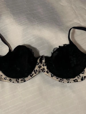 H&M Svart spets-bh med leopardkant 65A( 63-67cm) - Svart bh med genomskinlig spets och cool leopardmönstrad kant i beige och svart. Justerbara axelband och klassisk hakknäppning bak. Perfekt för dig som gillar detaljer och vill ha något extra under kläderna.
