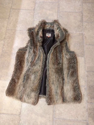 Brun pälsväst från ONLY, storlek L - Säljer en fluffig och snygg brun pälsväst från ONLY i storlek L. Västen har en cool, lite vild look med långa pälsstrån i olika bruna och beige nyanser. Perfekt att slänga över en hoodie eller tröja för extra stilpoäng.