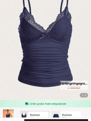 Mörkblå spetslinnetopp med rosett - Supersöt mörkblå linnetopp med tunna axelband, spetsdetaljer och liten rosett framtill. Toppen har blommönstrad spets över bysten och är figurnära med lätt rynkade partier. Perfekt att styla med jeans eller kjol för en trendig look.