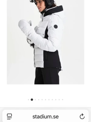 Svartvita skidjackan Everest 38 - Snygg svartvit skidjacka från Everest med huva och dragkedja framtill. Jackan har vadderad design, svarta detaljer på sidor och ärmar samt två dragkedjefickor. Perfekt för vinterns äventyr i backen.