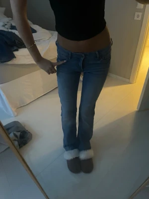 Blå bootcut jeans låg midja - Säljer ett par blå jeans med bootcut-snitt och låg midja. Jeansen har klassisk femficksdesign och är tillverkade i mjukt denimtyg. Passformen är normal och benen är lätt utsvängda nedtill för en snygg siluett.