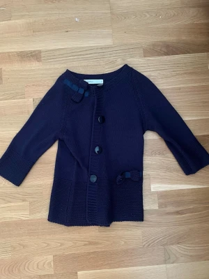 Mörkblå kofta Skovhuus - Mysig mörkblå kofta från Skovhuus med trekvartsärm och stora knappar framtill. söta dekorativa rosetter