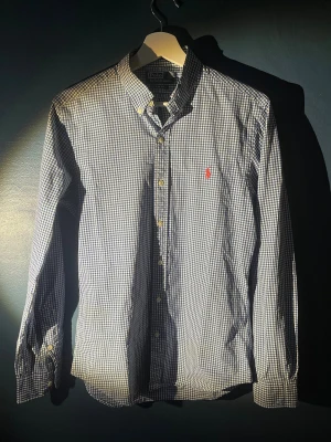 Blårutig skjorta från Polo Ralph Lauren - Säljer en blårutig skjorta från Polo Ralph Lauren i slim fit. Skjortan har klassisk krage, knappar hela vägen och det ikoniska röda broderade Polo-logot på bröstet. Tillverkad i mjuk bomull och har långa ärmar med knapp vid manschetten. Perfekt för dig som gillar stilrena detaljer.