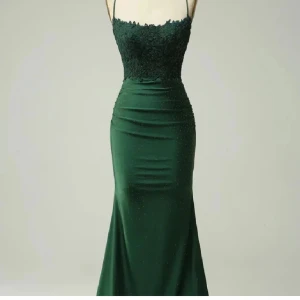 Mörkgrön balklänning  - Säljer en elegant mörkgrön långklänning med smala axelband och öppen rygg. Klänningen har spetsdetaljer upptill och små glittriga stenar. Figurnära passform och lätt utsvängd nedtill, perfekt för bal. storlek xs
