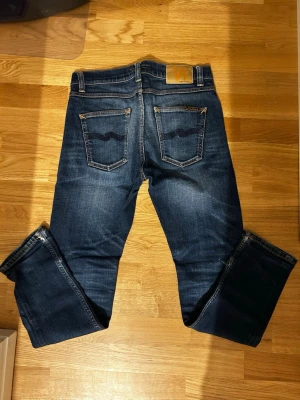 Mörkblå jeans från Nudie Jeans - Säljer ett par mörkblå jeans från Nudie Jeans. Jeansen har en rak passform och är tillverkade i slitstarkt bomullsmaterial. Jeansen är välanvända men har enligt mig väldigt snygg stonewash. Hör av er vid frågor och funderingar!! 