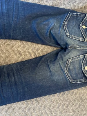 Blå jeans med kontrastsömmar - Säljer ett par blå jeans med snygga kontrastsömmar och markerade fickor både fram och bak. Jeansen har en klassisk femficksdesign och är tillverkade i slitstarkt denimtyg. Passformen är rak med lätt tvättade detaljer för en cool look.