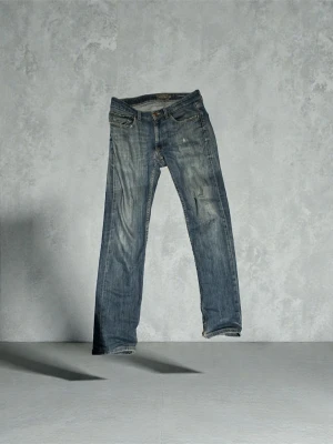 Blå jeans från Dressmann regular fit - Säljer ett par klassiska blå jeans från Dressmann i regular fit. Jeansen har en rak passform, fem fickor och snygga slitningar framtill för en cool look. Materialet är robust denim med kontrastsömmar. Perfekt för dig som gillar enkel och tidlös stil.