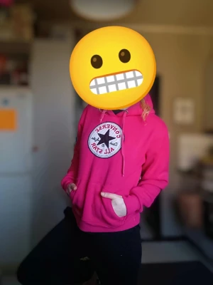 Rosa hoodie från Converse - Säljer en snygg rosa hoodie från Converse med det klassiska Chuck Taylor All Star-märket på bröstet. Hoodien har en stor ficka framtill och justerbar huva med snören. Perfekt för en avslappnad stil.