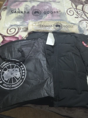 Svart dunjacka från Canada Goose - Svart dunjacka från Canada Goose med klassisk logga på ärmen och snygga detaljer. Jackan har lång ärm, dragkedja och knappar framtill. Fodrad med dun och fjädrar, samt avtagbar pälskant till huvan. Perfekt för kalla dagar och riktigt stilren.